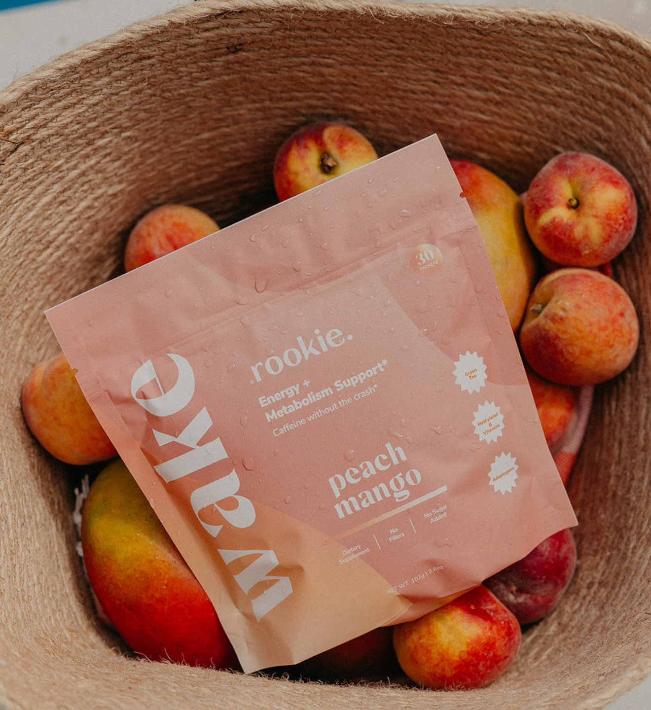 Peach mango flavored supplement packet in woven basket surrounded by fresh peaches.